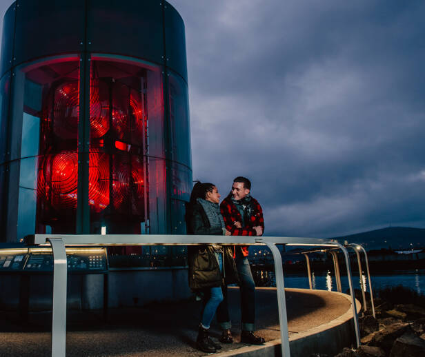 A couple smiling and chatting at the top of a lighthouse at night