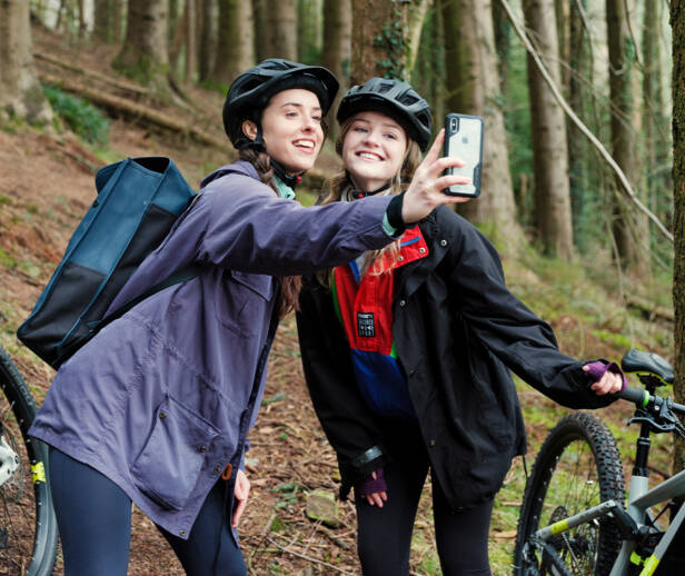 Two people in a forest with mountain bikes taking a selfie and smiling